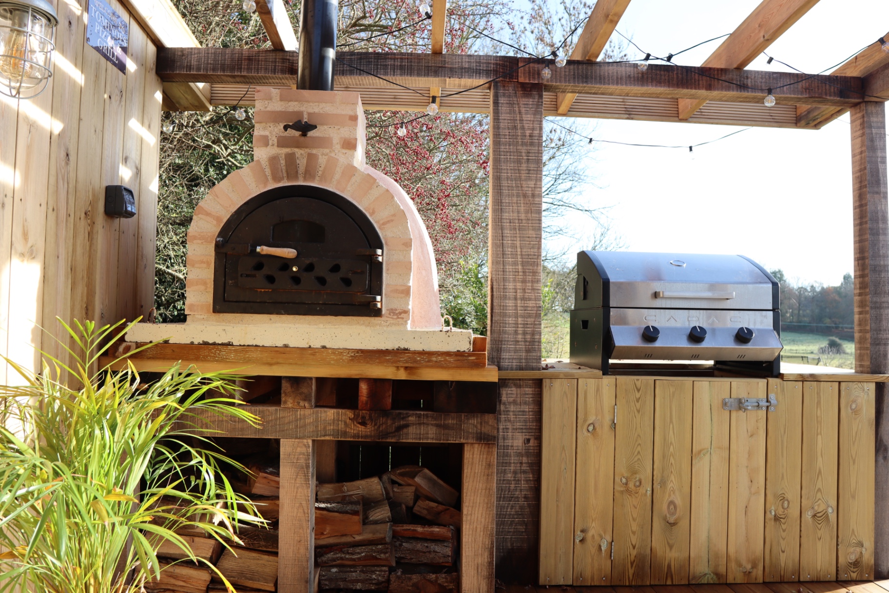 Wood-fired oven and barbecue station with firewood storage
